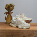Cream New Balance sneakers on wood next to wheat bundle, neutral sneaker footwear display
