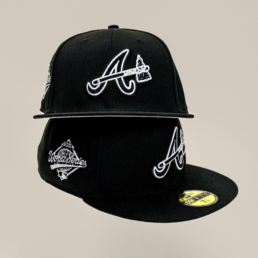 A black Atlanta Braves fitted cap with white embroidered logos, shown from multiple angles against a solid beige background.