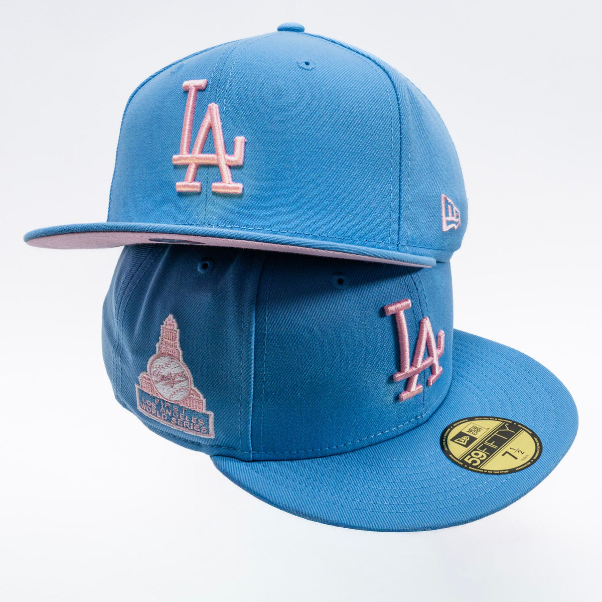 A blue Los Angeles Dodgers fitted baseball cap by New Era, featuring a pink embroidered 'LA' logo on the front and side, a pink 'Los Angeles' text patch on the side panel, and a gold size sticker on the brim.