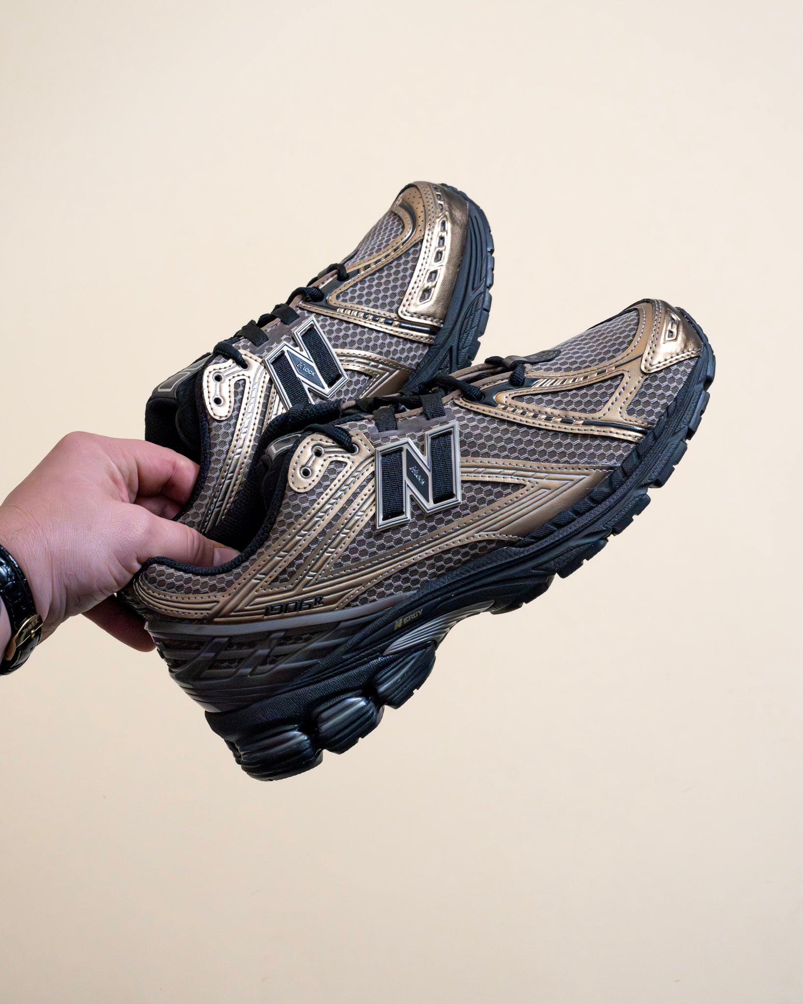 Hand holding metallic New Balance sneakers with black sole, footwear lifestyle product