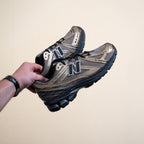 Hand holding metallic New Balance sneakers with black sole, footwear lifestyle product
