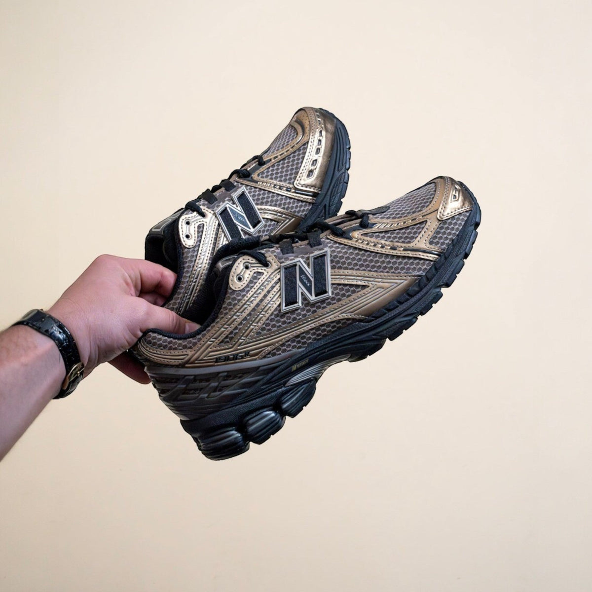 Hand holding metallic New Balance sneakers with black sole, footwear lifestyle product