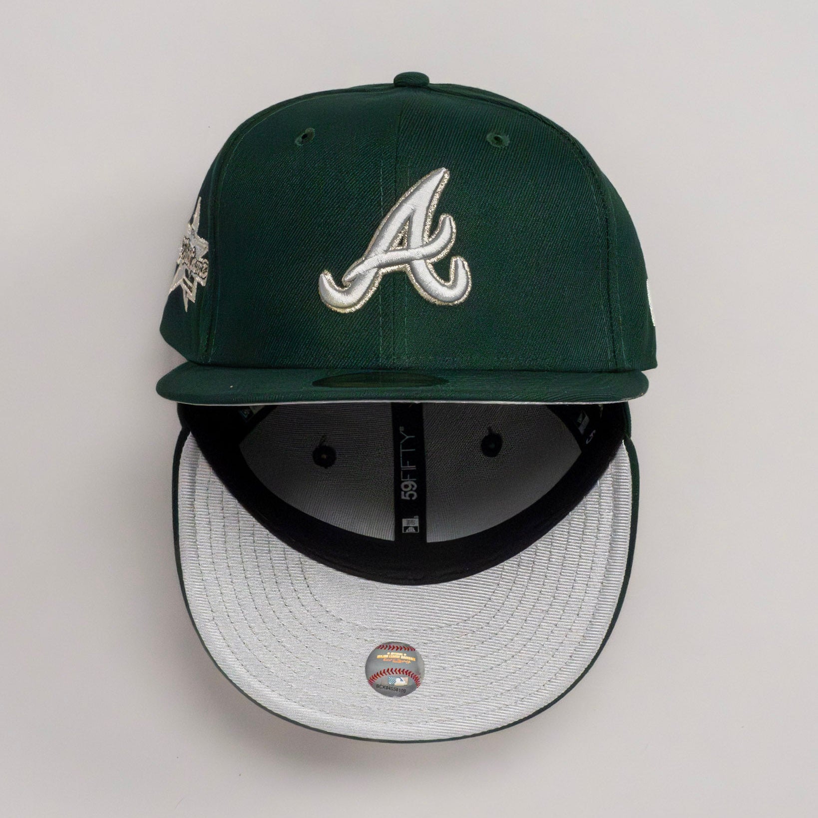 Dark green New Era fitted cap with embroidered A logo, side patch, and white underbrim.