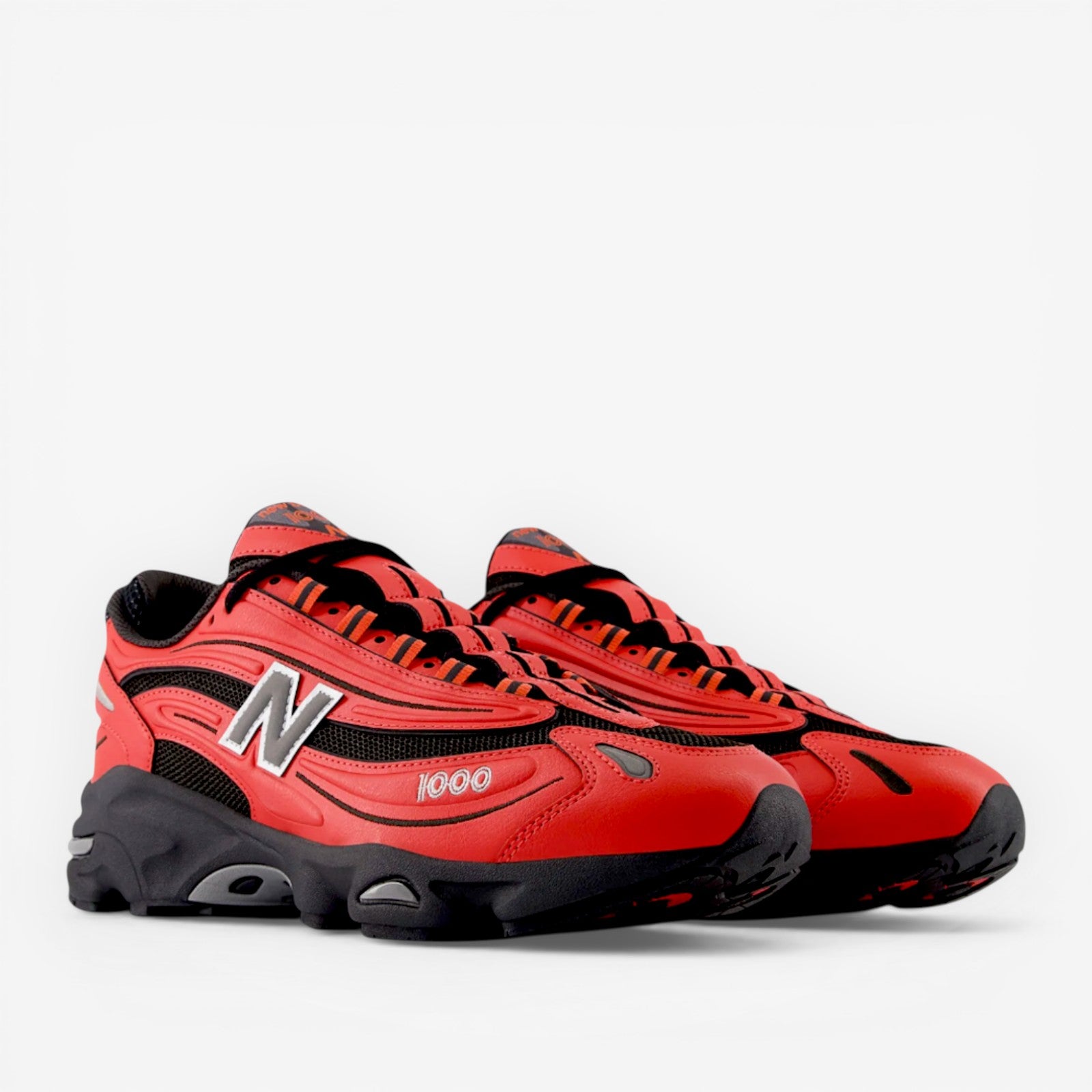 Red and black New Balance 1000 sneakers, athletic footwear with bold N logo and mesh accents
