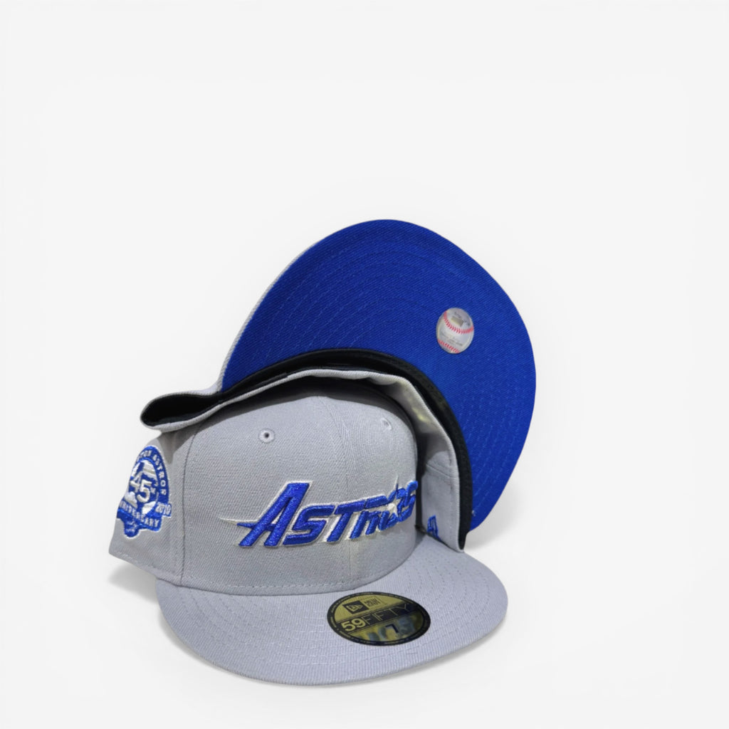 New Era fitted cap in grey and blue with Astros logo, anniversary patch, and baseball graphic under brim.