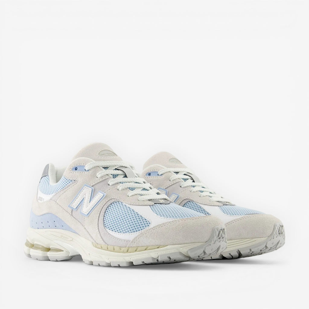 Light blue and white New Balance sneakers with suede and mesh paneling, side view.