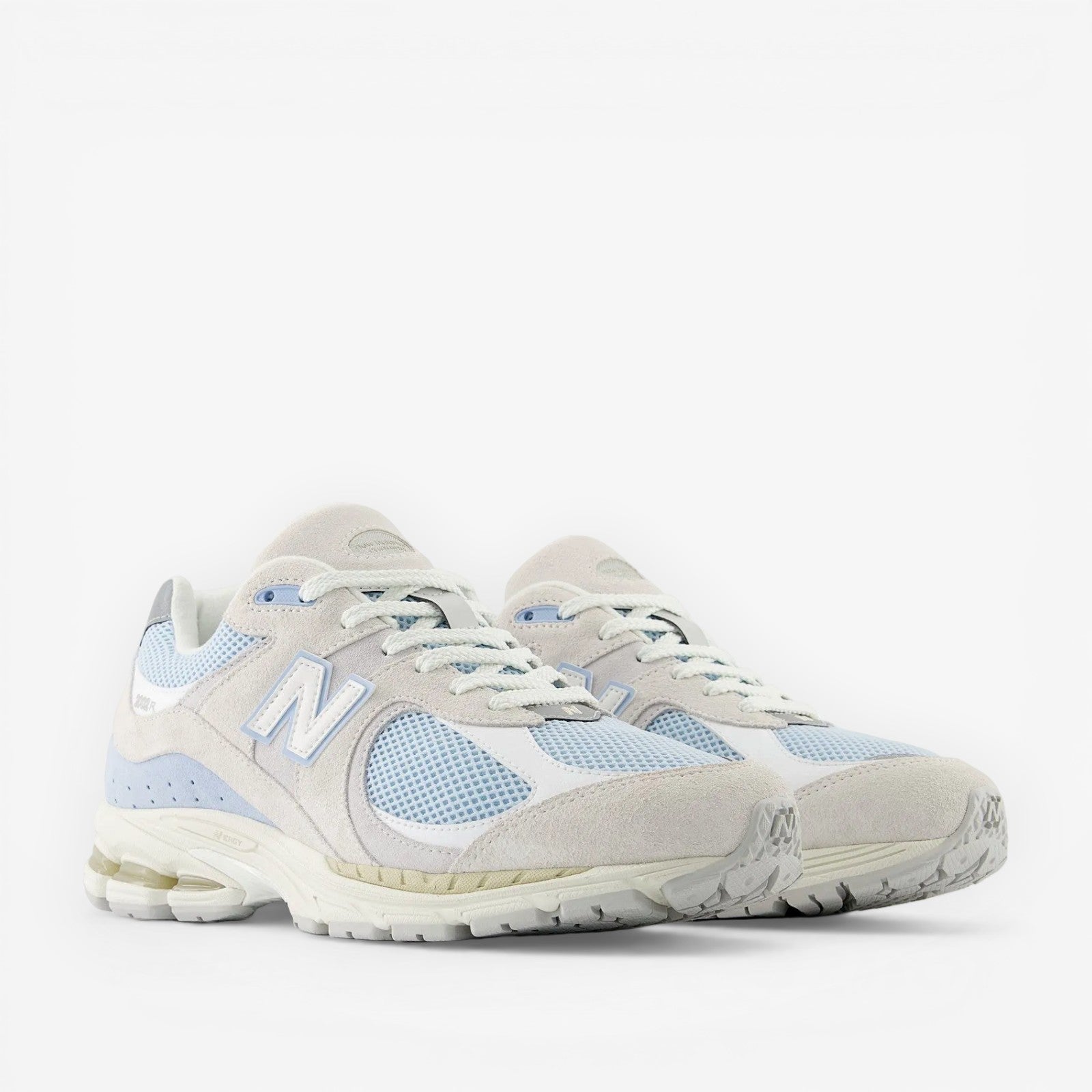 Light blue and white New Balance sneakers with suede and mesh paneling, side view.