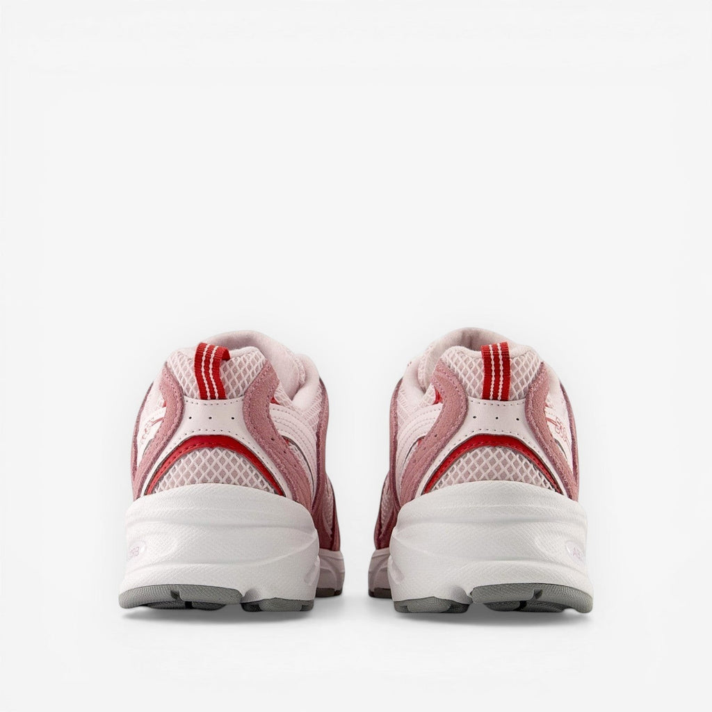 rear view of pink and white new balance sneakers with mesh panels and red heel accents